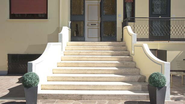 A building with a set of stone steps leading to a door with glass panels and a metal gate. - Domus in Viridi (Rome)