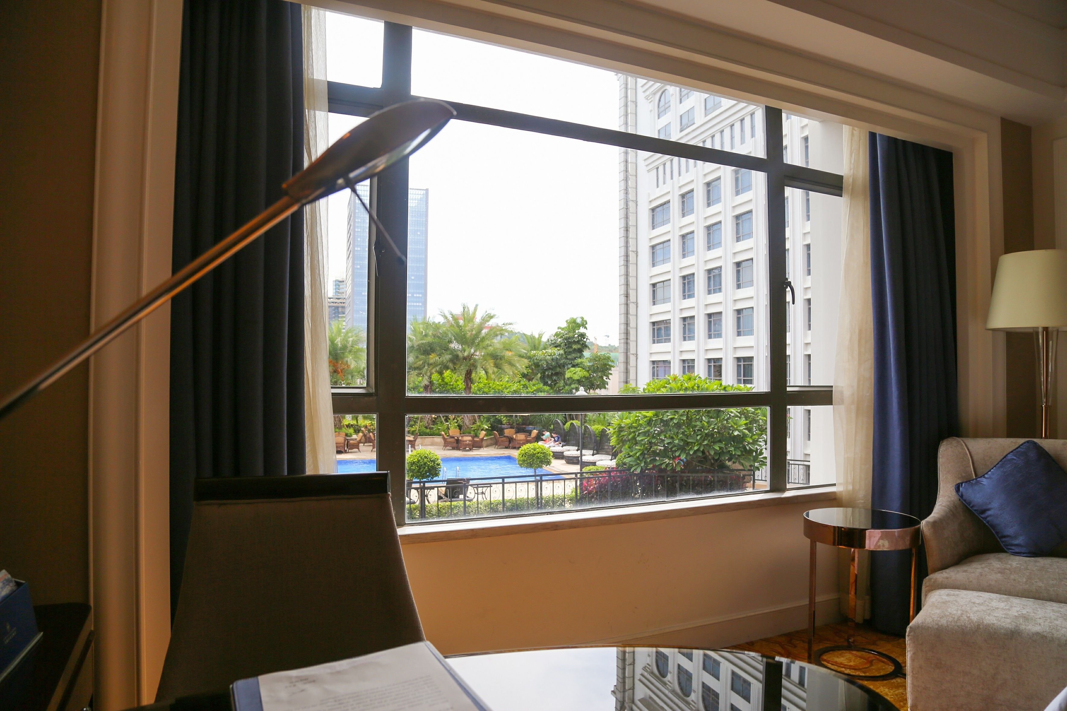 A hotel room with a large window, a sofa, a side table, and a lamp.