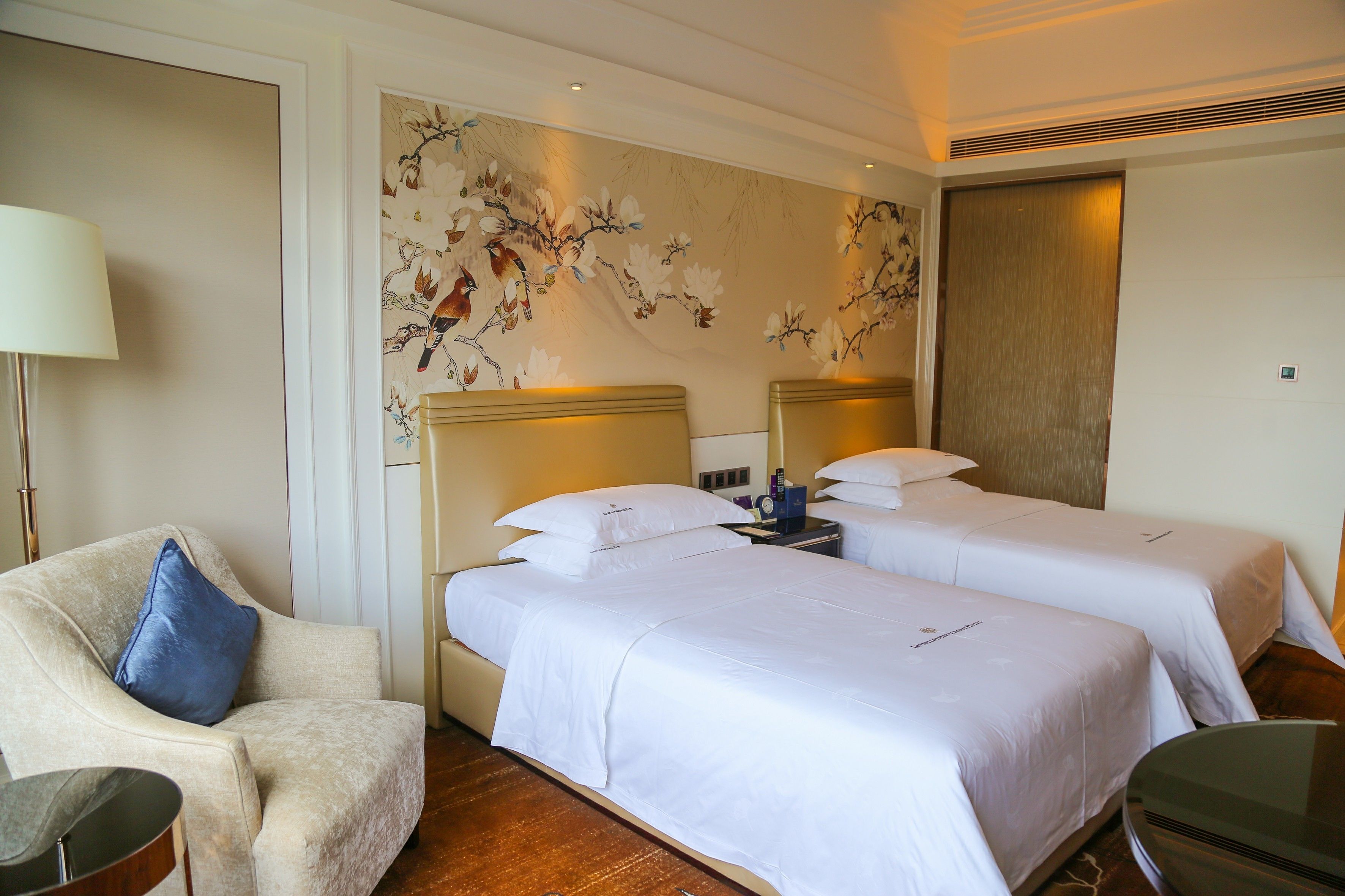 Ein Hotelzimmer mit zwei Einzelbetten, einer Couch, einer Lampe und einer Wanddekoration.