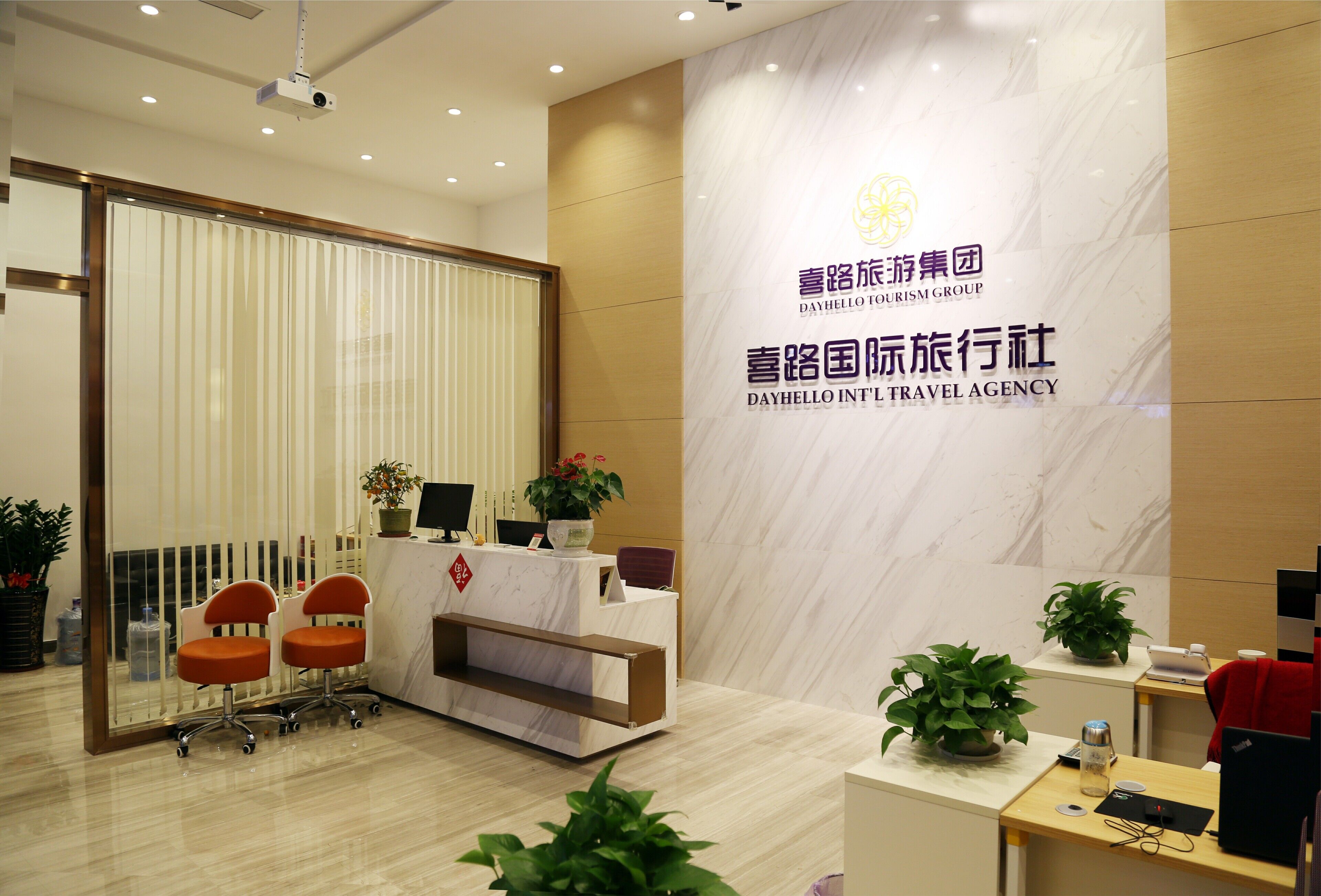 A reception area with a reception desk, two orange chairs, a potted plant, and a large sign with the agency's name.