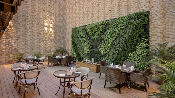 An outdoor dining area with wicker chairs and tables, a brick wall, and a green vertical garden. - Country Inn & Suites by Radisson Zirakpur (Dera Bassi)