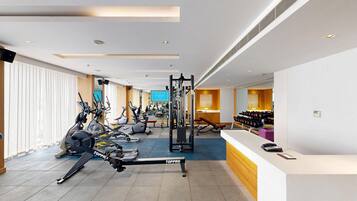 A modern gym with various exercise equipment, a reception desk, and a large mirror.