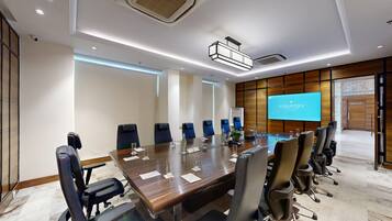 A conference room with a long table, chairs, a projector screen, and a wooden accent wall.