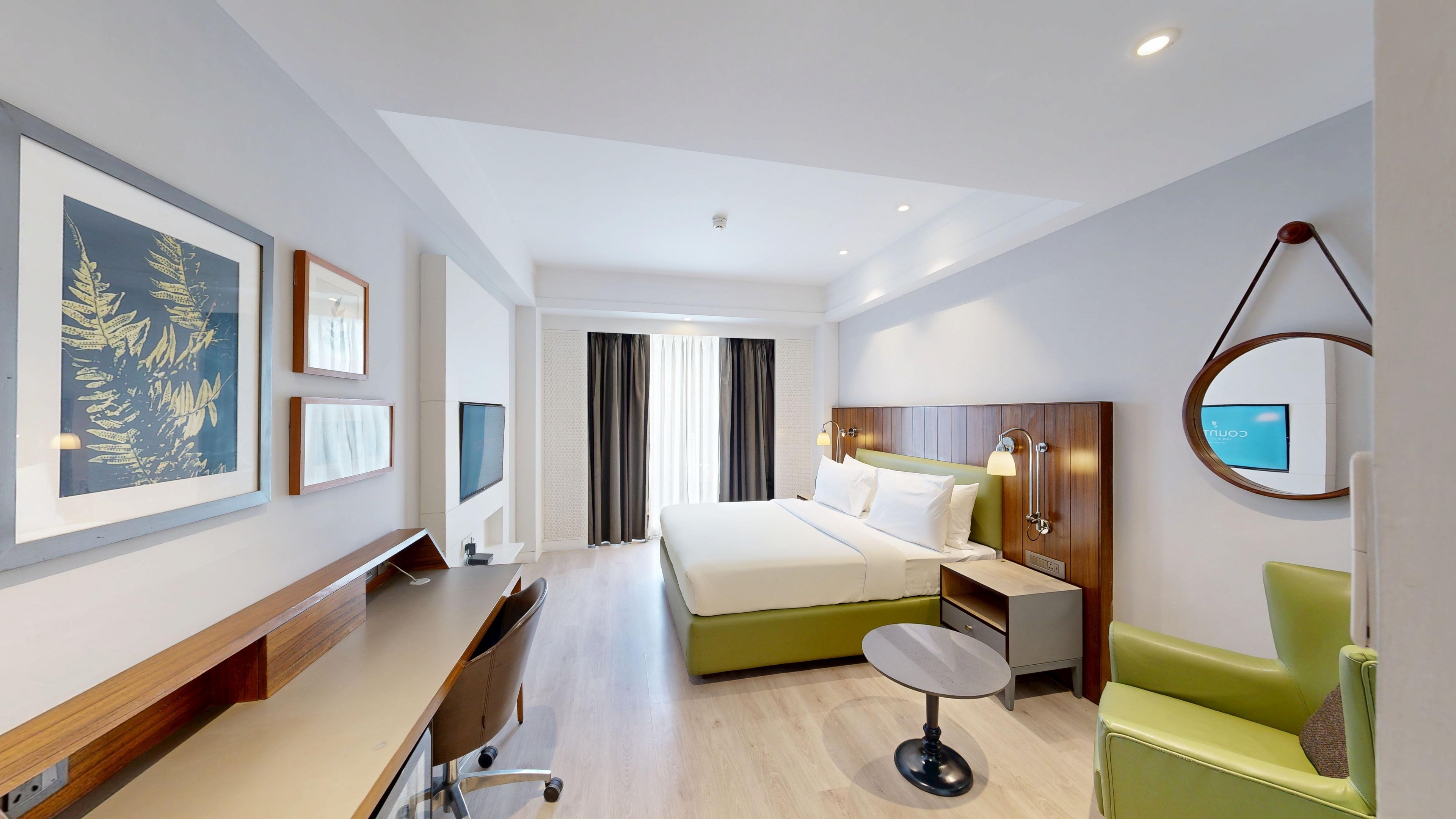 A hotel room with a bed, a desk, a chair, a TV, and artwork on the walls.