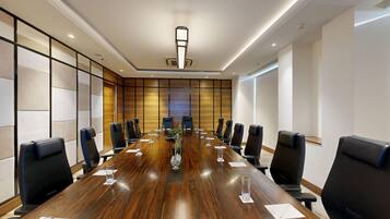 A conference room with a long wooden table, black chairs, and a modern ceiling design.