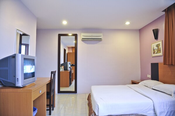 A hotel room with a bed, a desk with a television, a mirror, an air conditioning unit, and a picture on the wall.