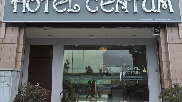 A hotel entrance with a sign reading "HOTEL CENTUM" and a reflection of palm trees in the glass door.