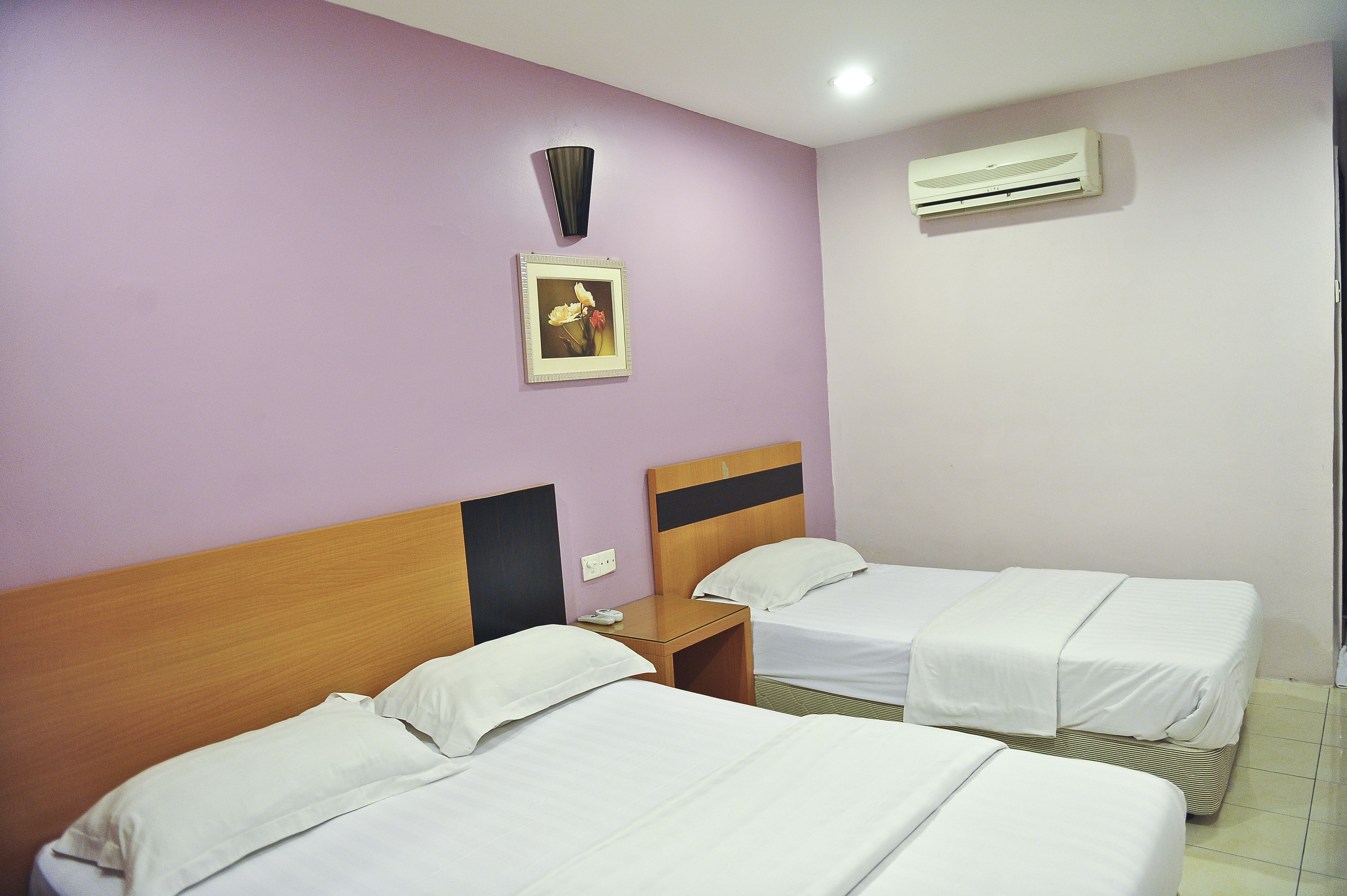 A hotel room with two beds, a nightstand, a wall-mounted air conditioner, and a framed picture on the wall.