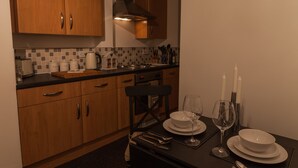 A modern kitchen with wooden cabinets, a black countertop, and a dining area set for two with white plates and glasses. - Station Suite - Simple2let Serviced Apartments (Halifax)