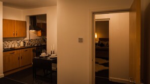 A compact kitchen with wooden cabinets, a dining table set for two, and a doorway leading to a bedroom. - Station Suite - Simple2let Serviced Apartments (Halifax)