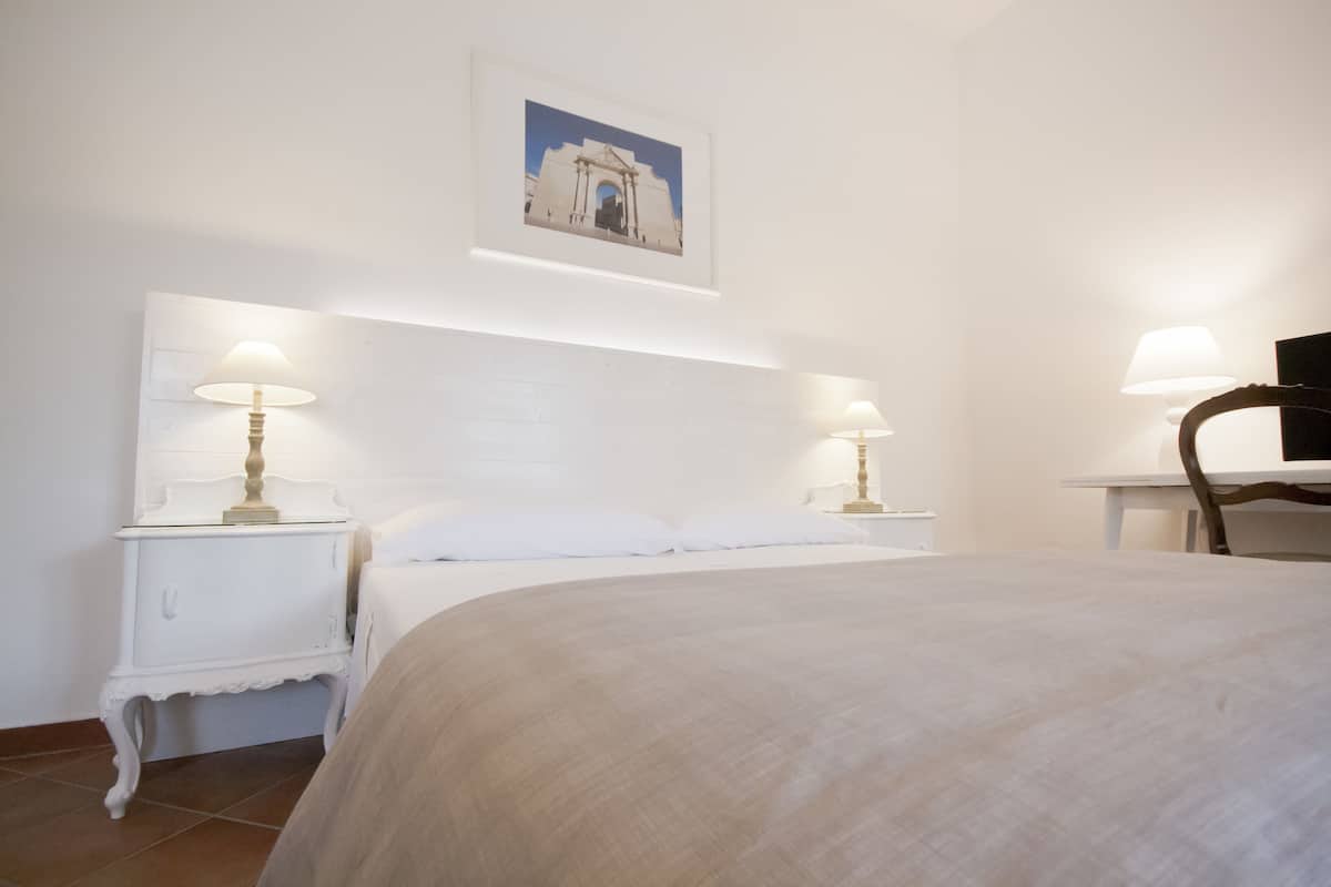 Une chambre à coucher avec un grand lit, deux tables de chevet avec des lampes, une chaise et un tableau accroché au mur.