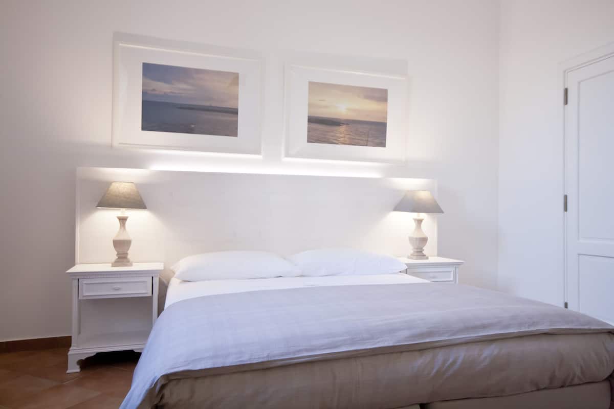 Une chambre à coucher avec un lit, deux tables de chevet avec des lampes et deux tableaux encadrés accrochés au mur.