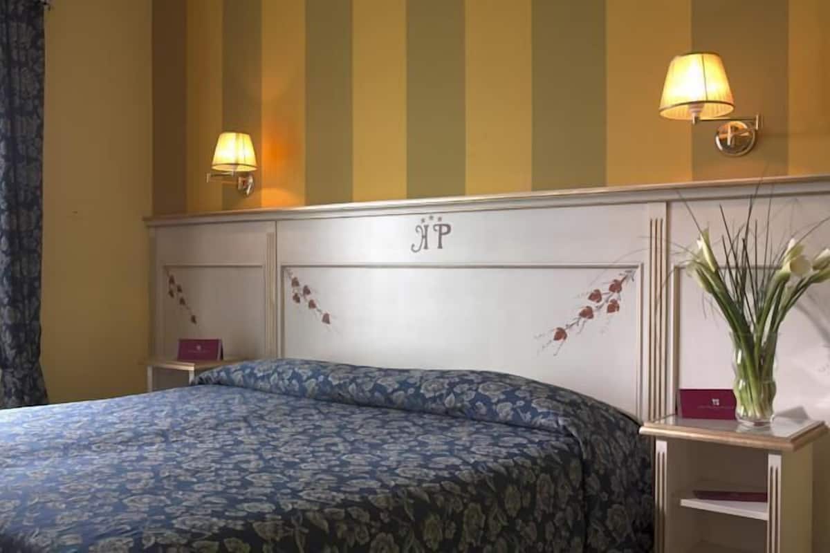 Hotelkamer met een bed, twee nachtkastjes, een lamp, een vaas met bloemen en een wand met verticale strepen en een bord.