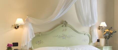 A bedroom with a canopy bed, floral headboard, bedside lamps, and a nightstand with a vase.