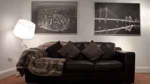 A living room with a black leather sofa, a throw blanket, and two framed cityscape photographs on the wall. - Central Suite - Simple2let Serviced Apartments (Halifax)