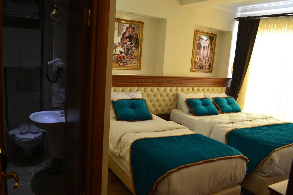 A hotel room with two beds, a bathroom, and a painting on the wall.
