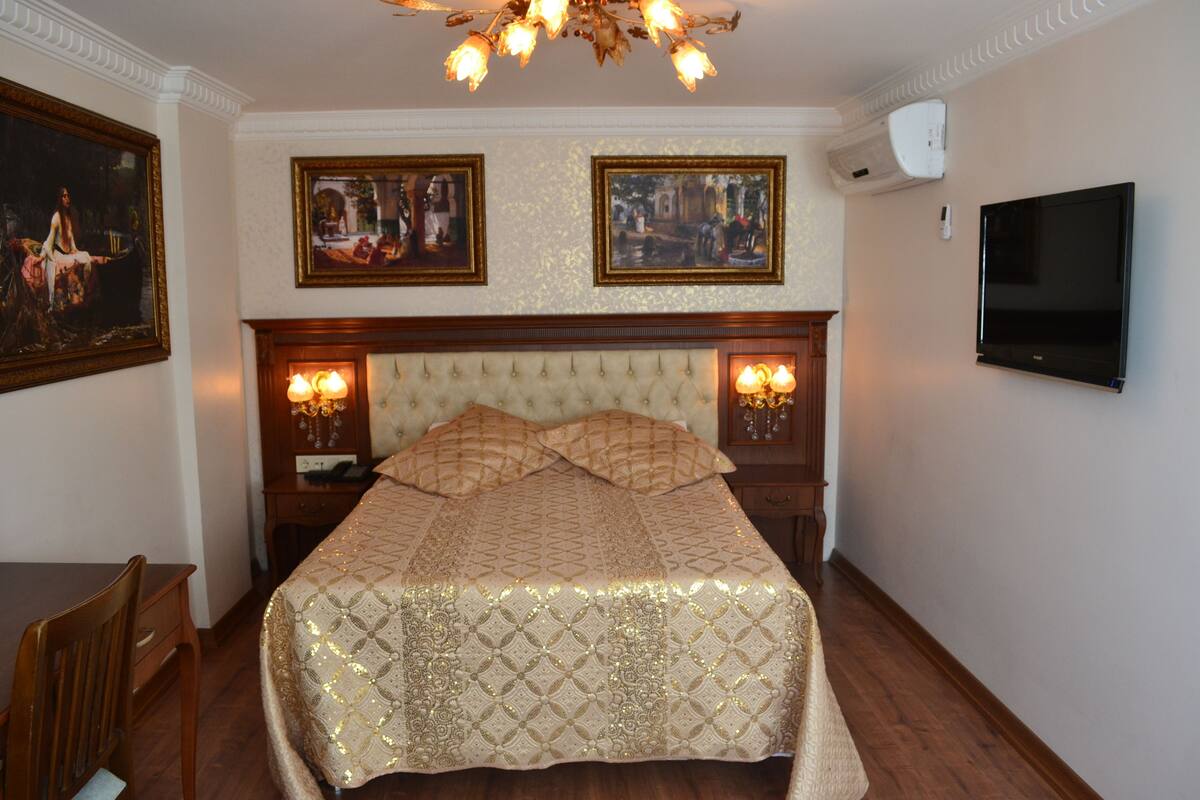 A bedroom with a large bed, two wall-mounted lamps, a flat-screen TV, and framed pictures on the wall.