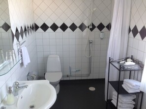 A bathroom with a white sink, toilet, and shower. There is a towel rack with folded towels.