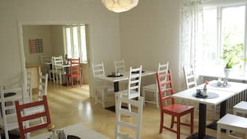 A dining area with white tables and chairs, a hanging light fixture, and a view of greenery outside.