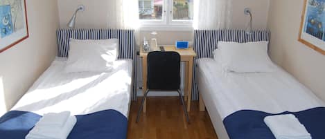 Una habitación con dos camas individuales, un escritorio, una silla y un ventanal con cortinas.
