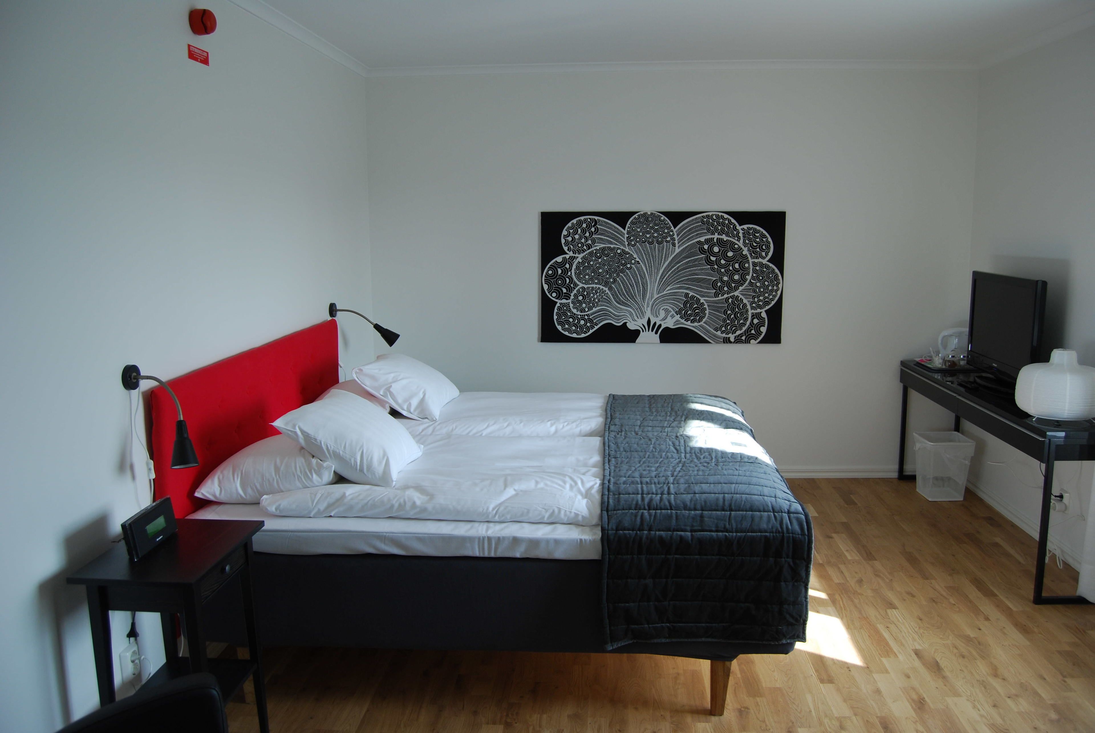 Un dormitorio con cama, escritorio, silla, una obra de arte en la pared y televisor.