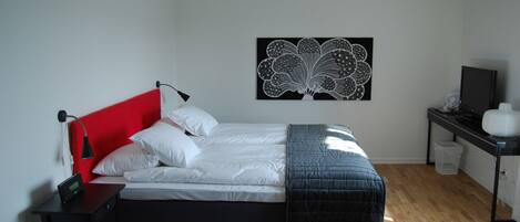 Un dormitorio con cama, escritorio, silla, una obra de arte en la pared y televisor.