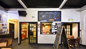 A reception area with a chalkboard displaying tourist attractions, a seating area with chairs, and a signboard. - Arsenal Tavern Backpackers (London)