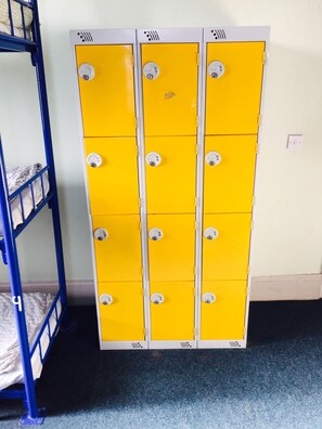 Een aantal gele lockers met verschillende vakken, een blauw stapelbed en een vloerbedekking.