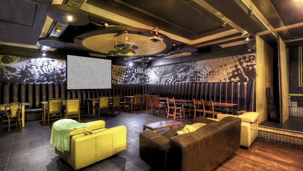 A spacious room with a large screen, comfortable seating, and a stage area. - Arsenal Tavern Backpackers (London)