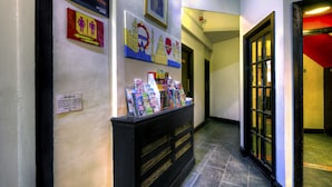 A hallway with a reception desk displaying brochures and a sign indicating the location of restrooms. - Arsenal Tavern Backpackers (London)