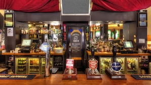 A bar with multiple taps, a cash register, and a menu board. - Arsenal Tavern Backpackers (London)