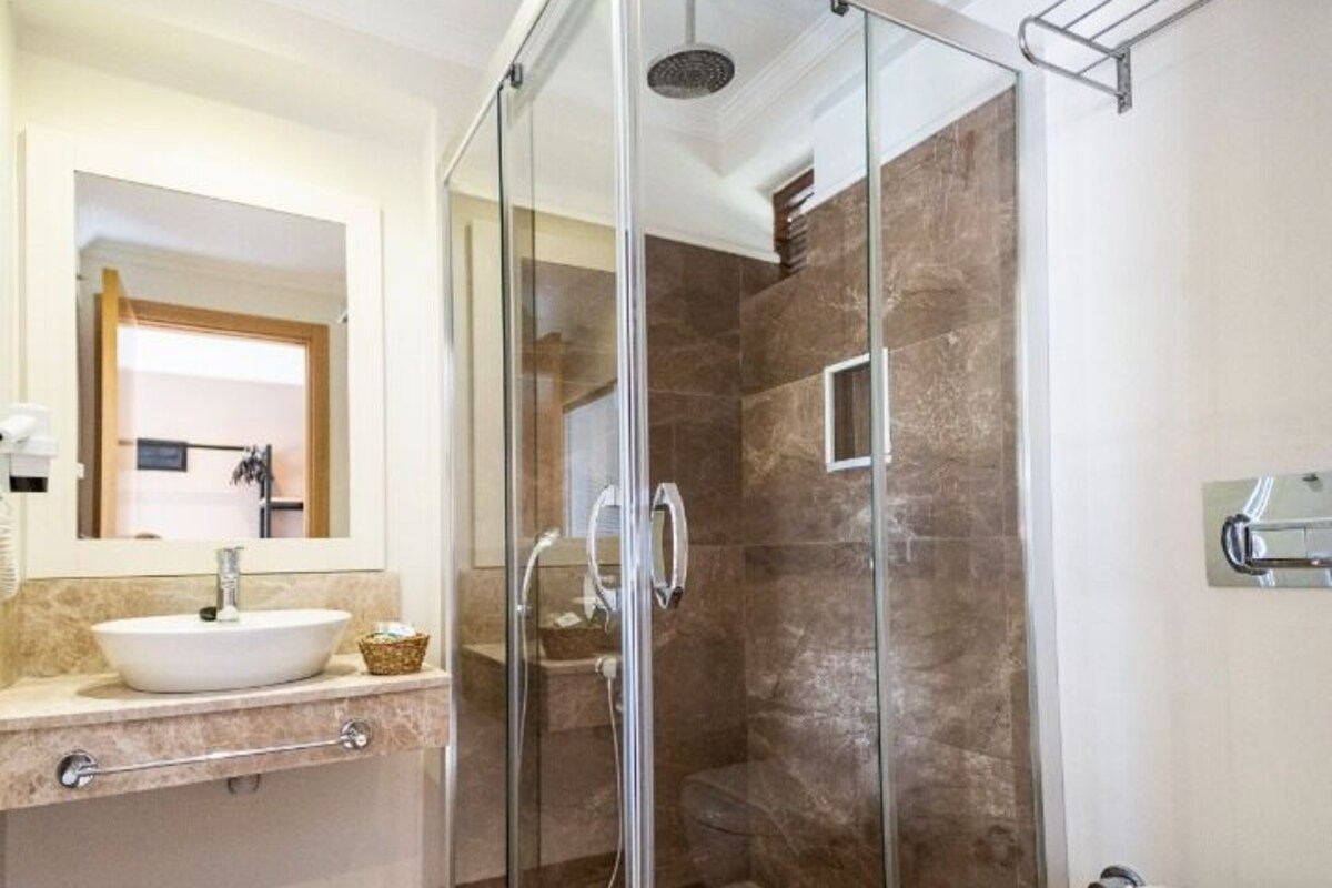 Un baño moderno con ducha envuelta en vidrio, un lavamanos blanco y un inodoro.