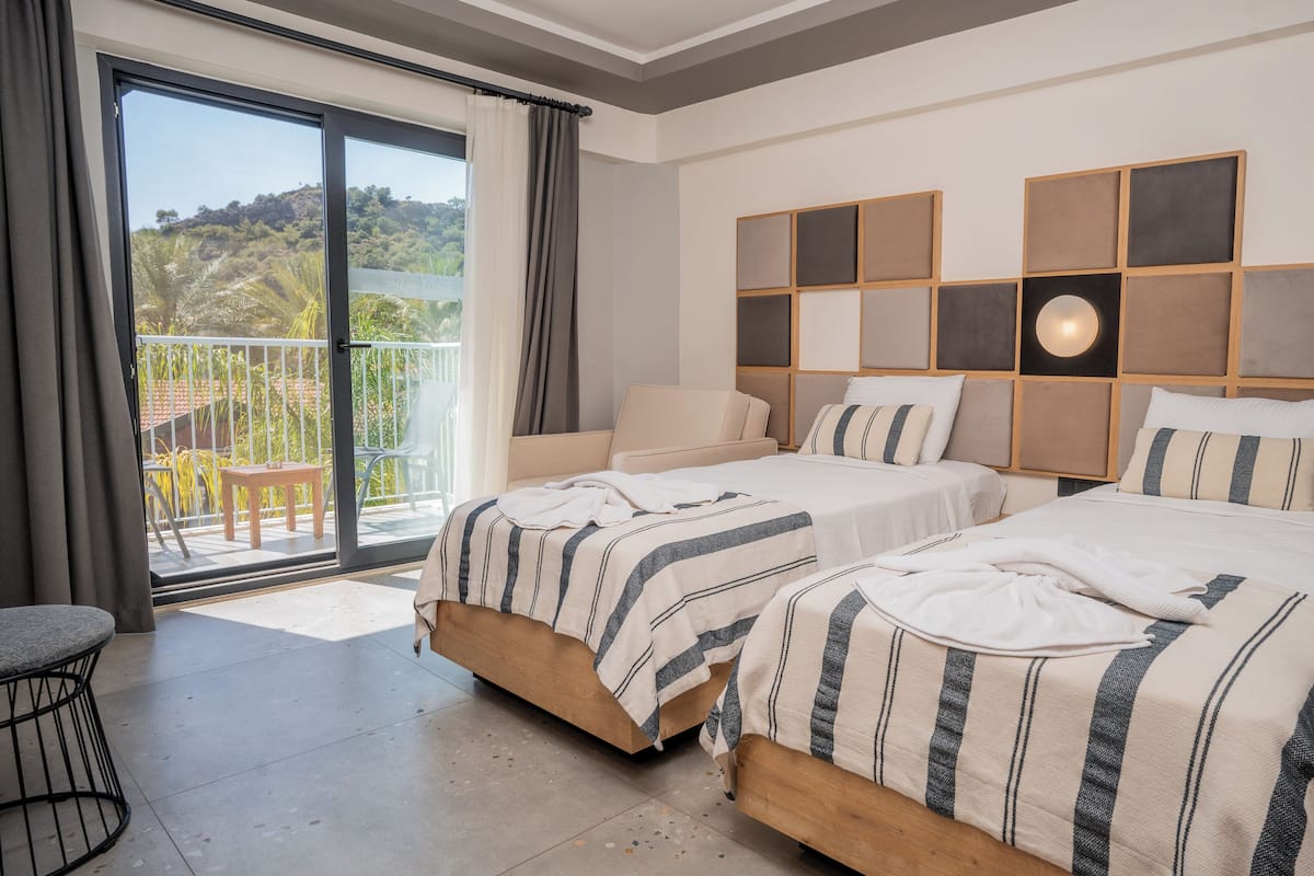 A hotel room with two beds, a balcony, and a view of a hillside.