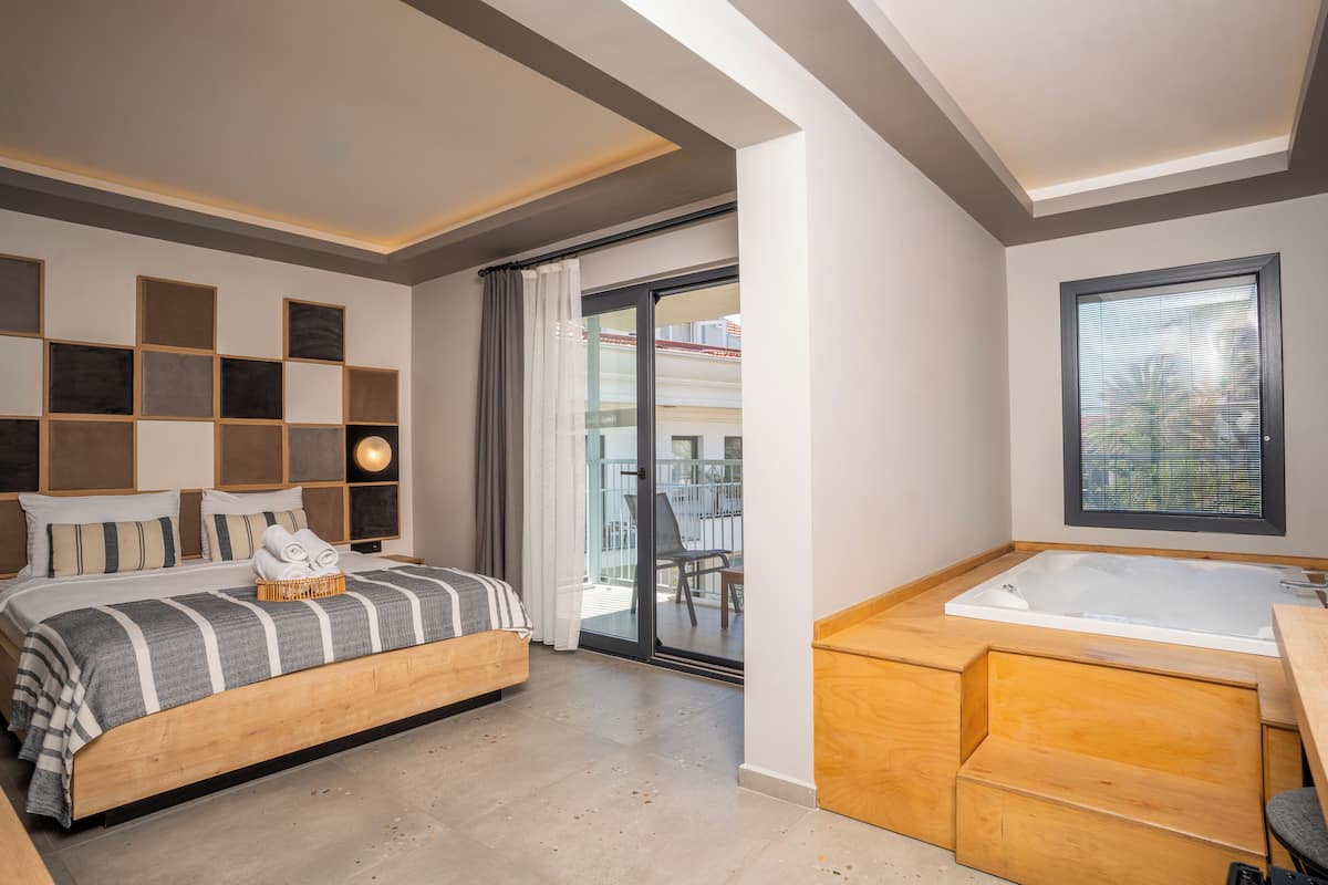 A modern bedroom with a large bed, a built-in bathtub, and a balcony with a view.
