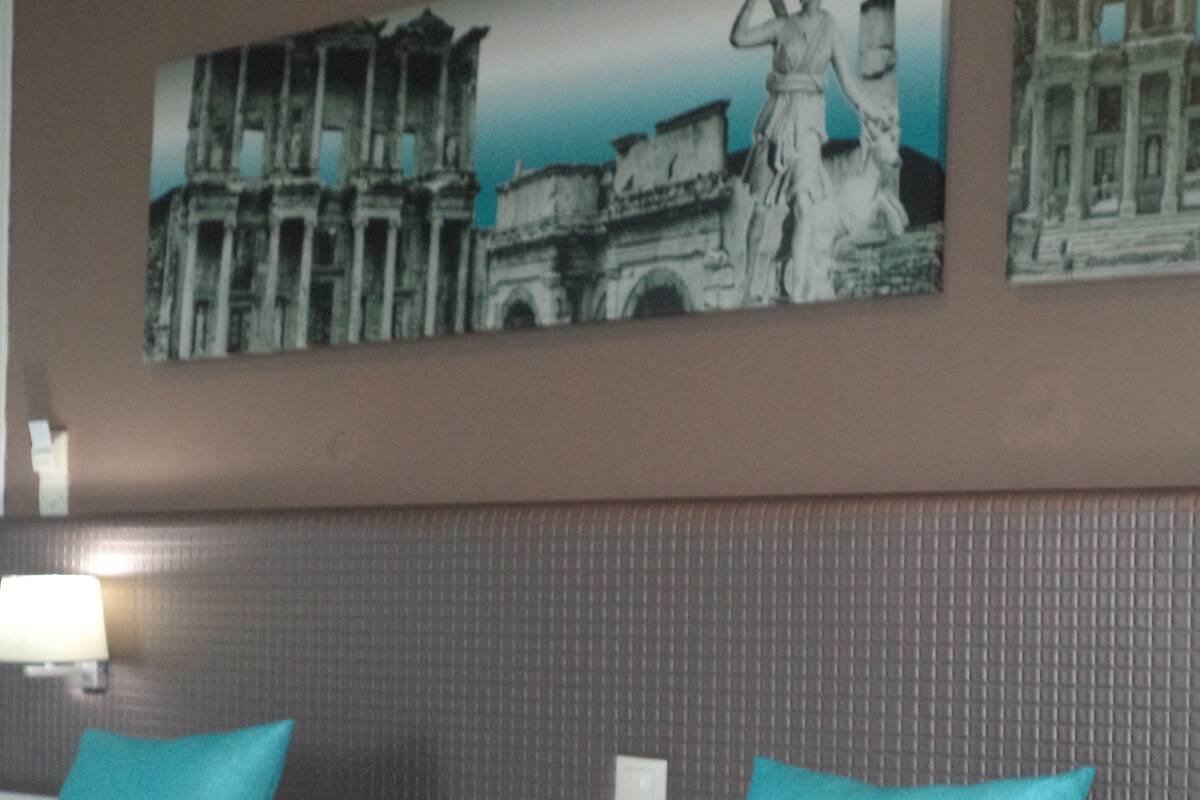 Quarto de hotel com duas camas, cada uma com travesseiro azul e edredom branco. Há uma luminária fixada na parede ao lado esquerdo da cama.