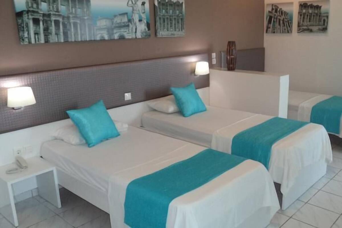 Quarto de hotel com duas camas de solteiro, uma mesa de cabeceira e uma luminária fixada na parede.
