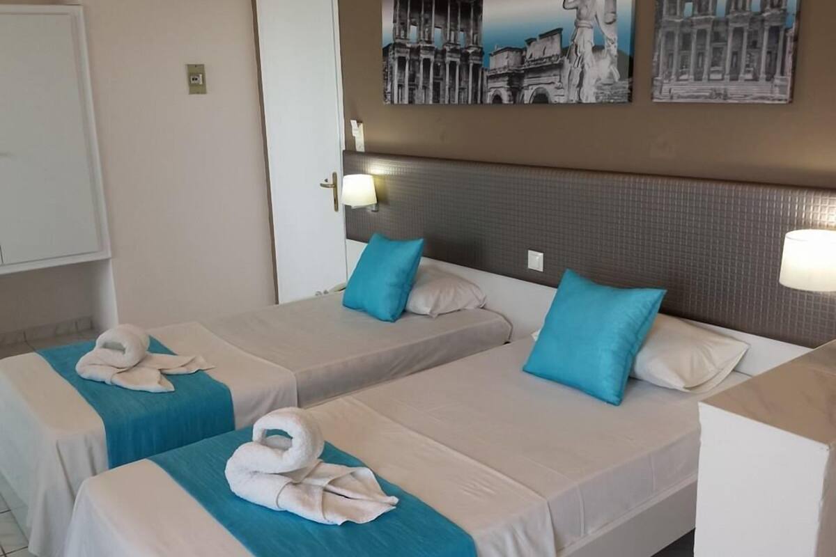 Quarto de hotel com duas camas, cada uma com colcha e travesseiros azuis, e cabeceira com textura.