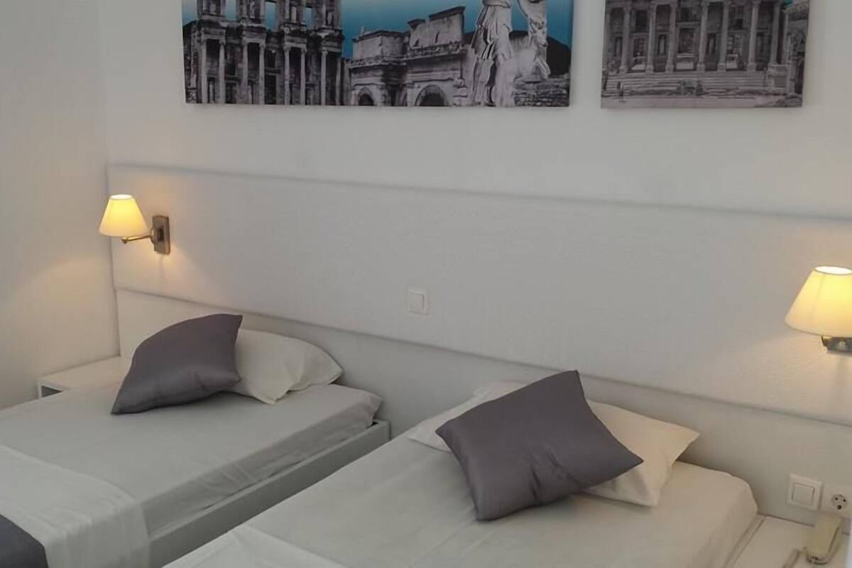 Quarto de hotel com duas camas de solteiro, cada uma com travesseiro e abajur.