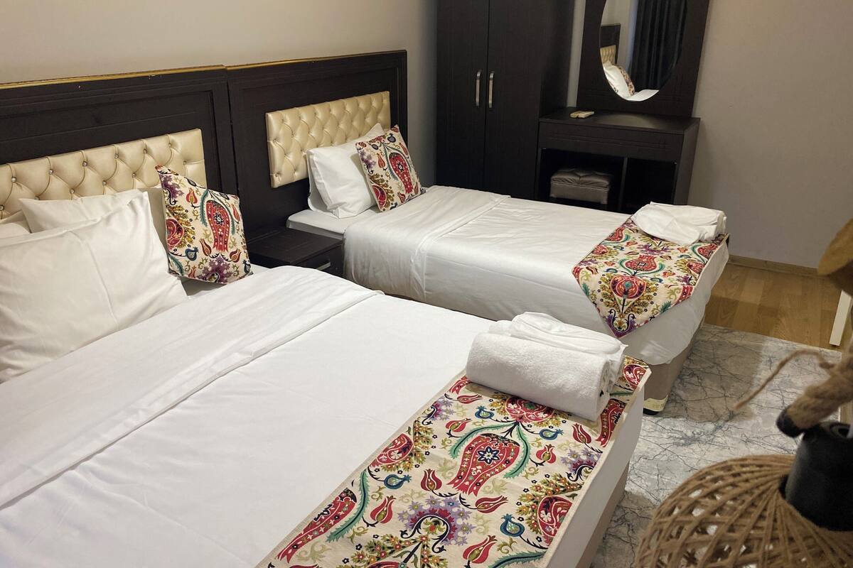 A hotel room with two beds, a dark wardrobe, a mirror, and a small bench with a towel.