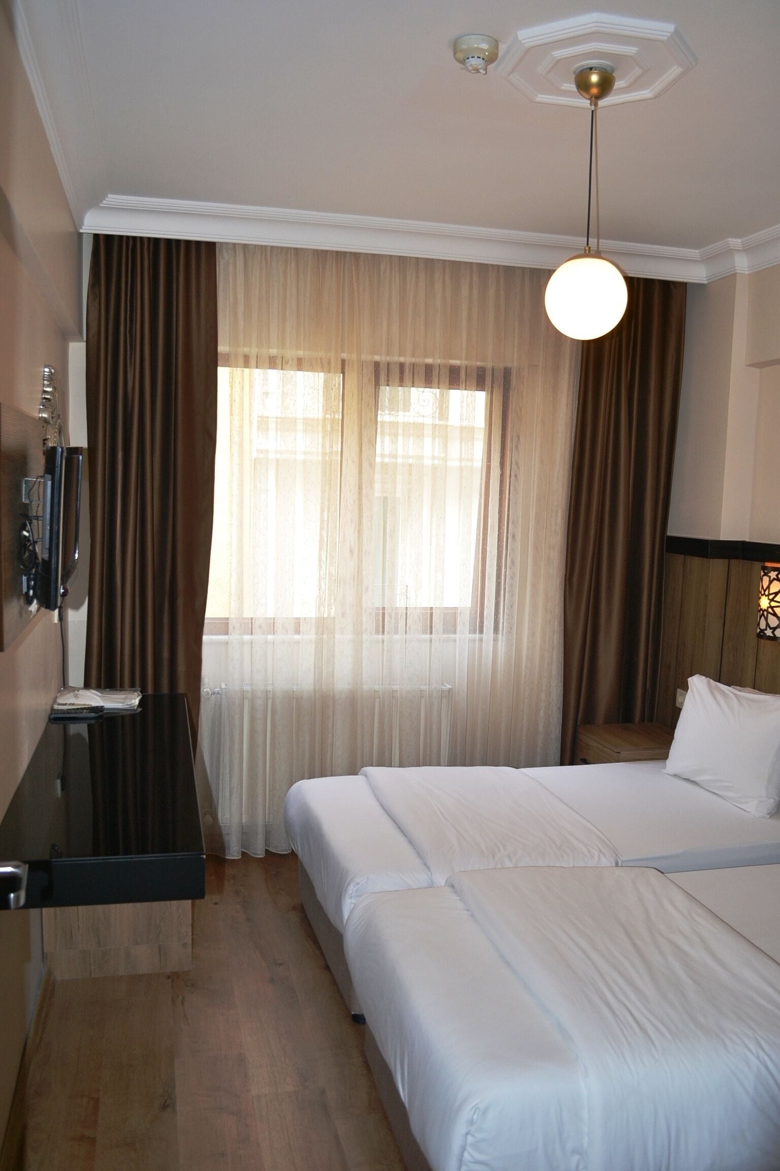 A hotel room with a bed, a desk, and a window with curtains.