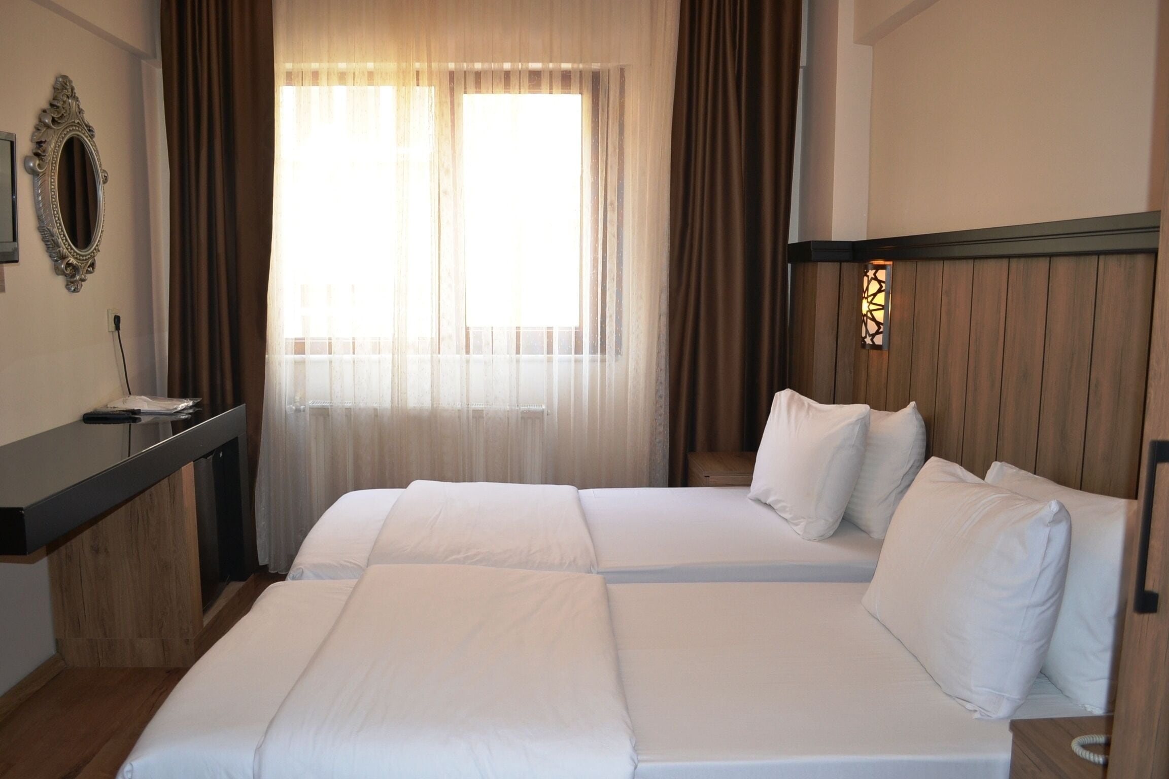 Une chambre d’hôtel avec deux lits, un bureau et une fenêtre avec des rideaux.