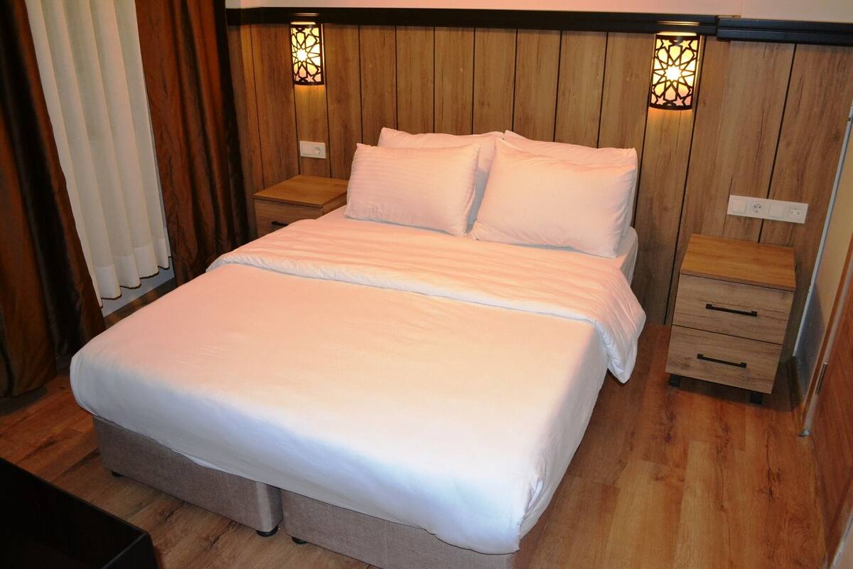 A neatly made bed with white linens in a room with wooden paneling and two bedside tables with lamps.