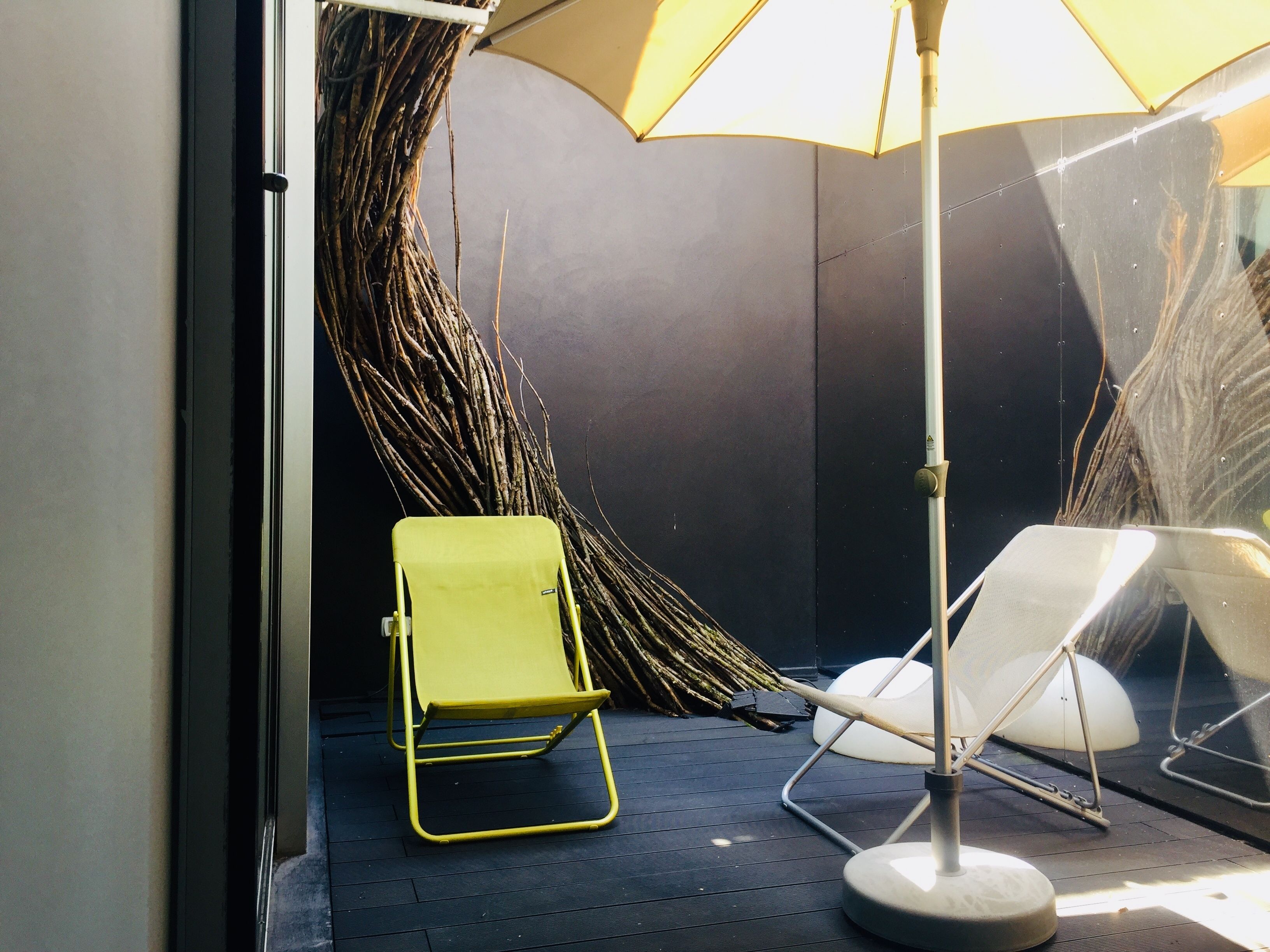 Un espace extérieur moderne avec des sièges, comprenant une chaise jaune et une chaise blanche, placés sous un grand parasol.