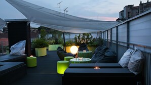 Une terrasse sur le toit, aménagée avec des coins salon, une table et un éclairage d’ambiance.