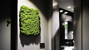 Une salle de bain moderne avec un mur recouvert de mousse verte, un lavabo blanc et un miroir.