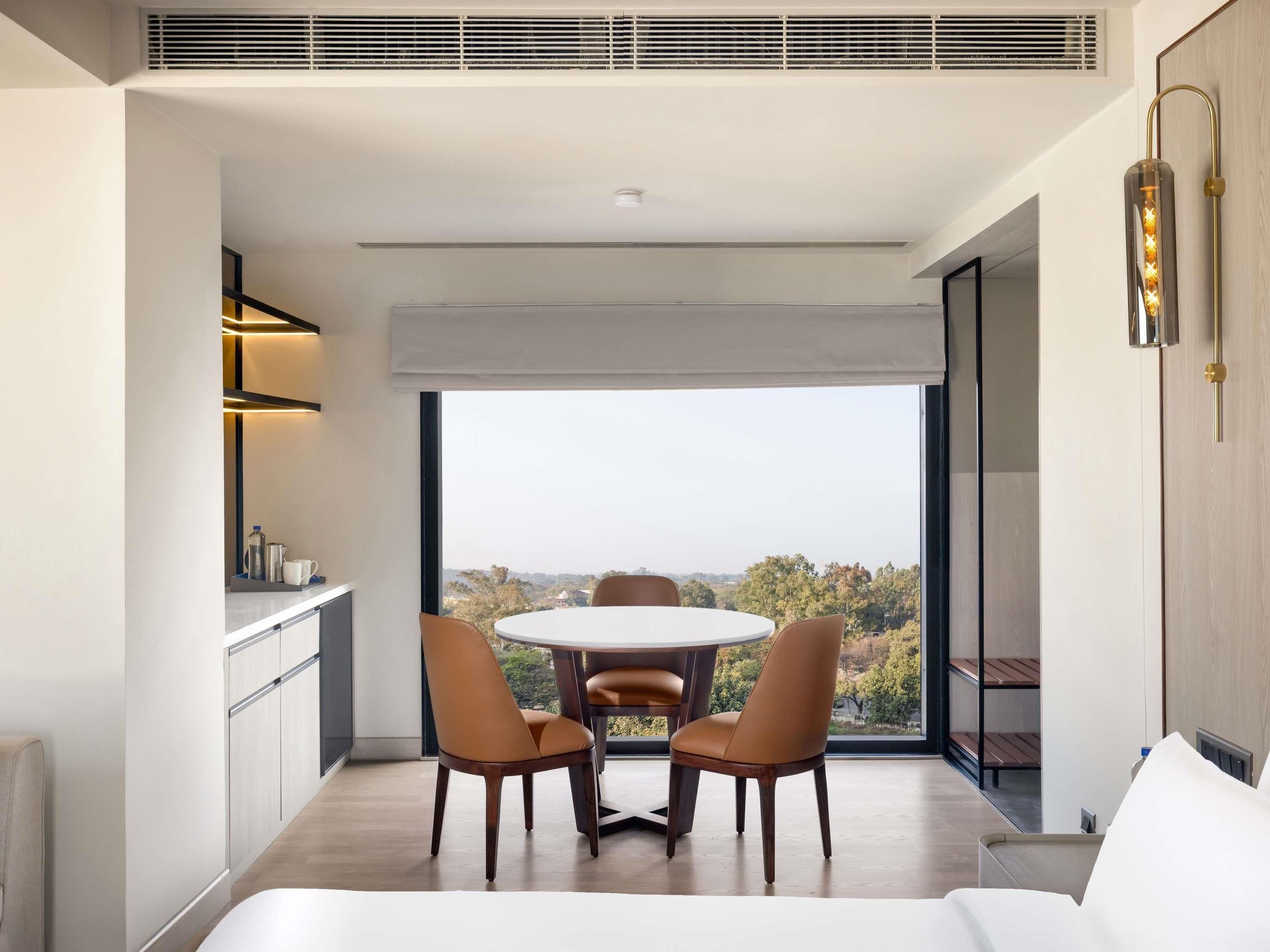 A modern dining area with a round table and two chairs, a kitchen with a built-in stove, and a large window offering a view of the outdoors.
