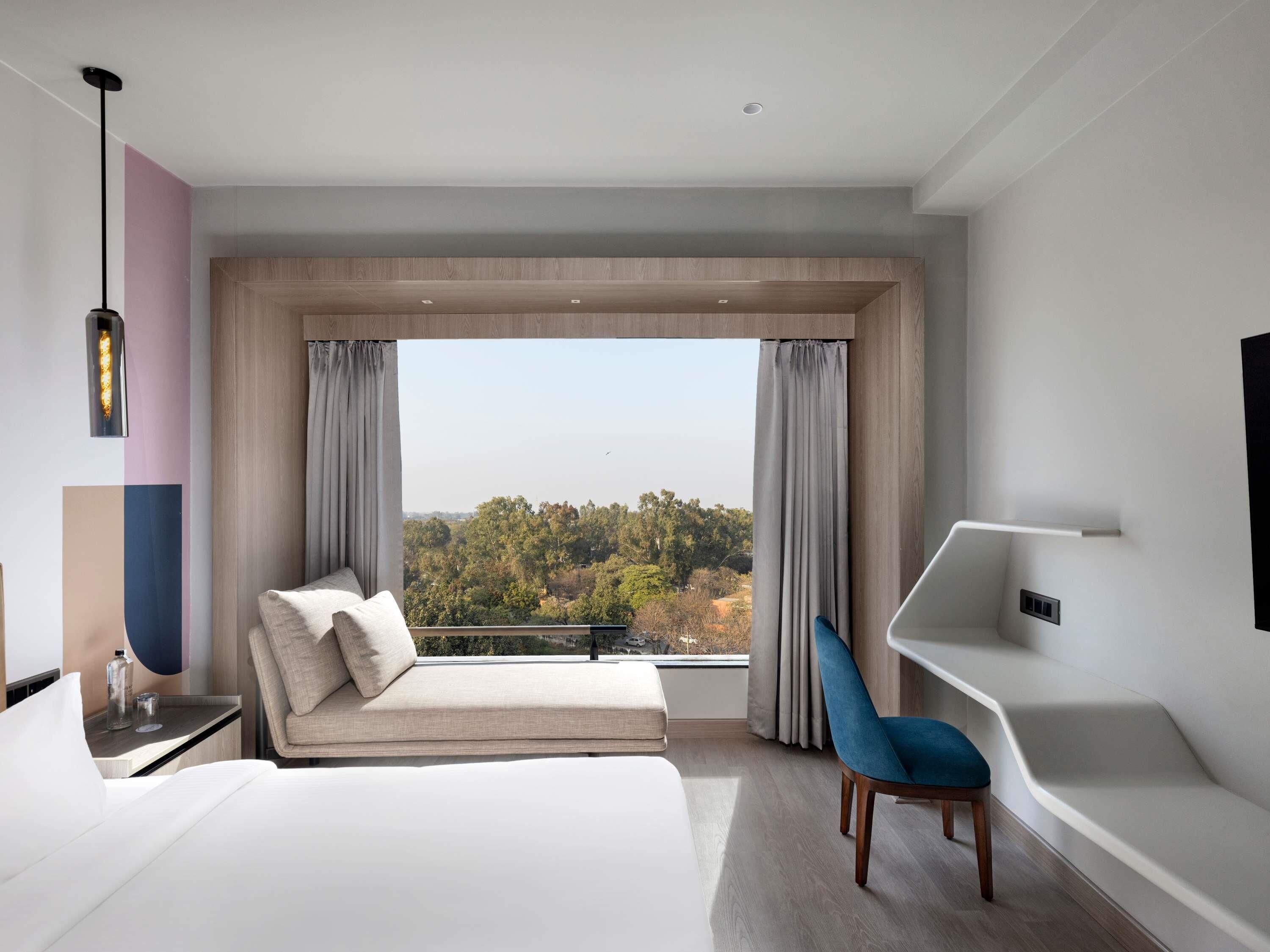 A modern hotel room with a large bed, a seating area with a view, and a desk with a chair.