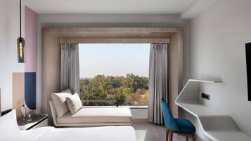 A modern hotel room with a large bed, a seating area with a view, and a desk with a chair.