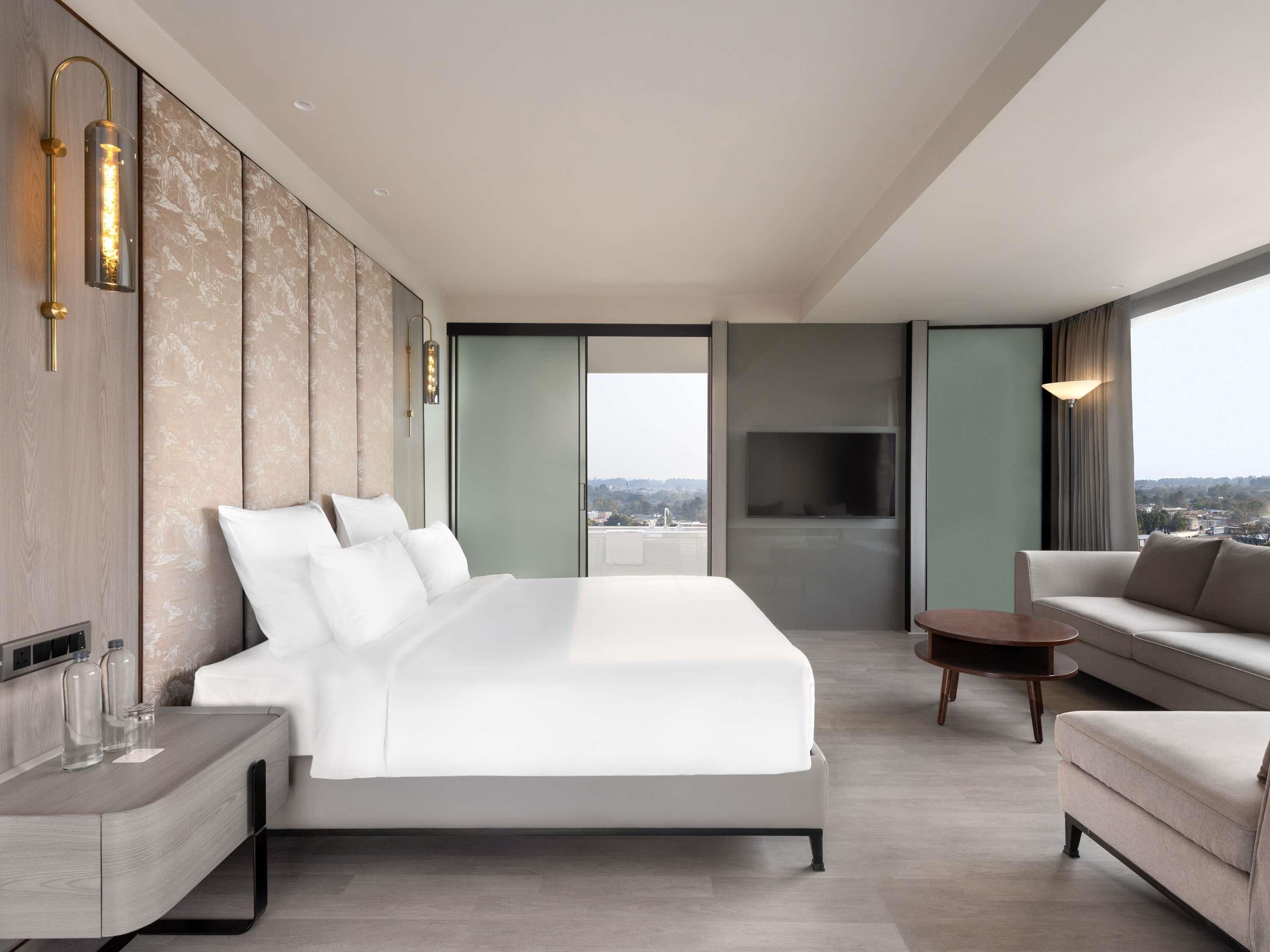 Een moderne hotelkamer met een groot bed, een bank, een televisie en uitzicht over de stad.