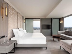 A modern hotel room with a large bed, a sofa, a TV, and a view of the city. - Mercure Chandigarh Tribune Chowk (Chandigarh)